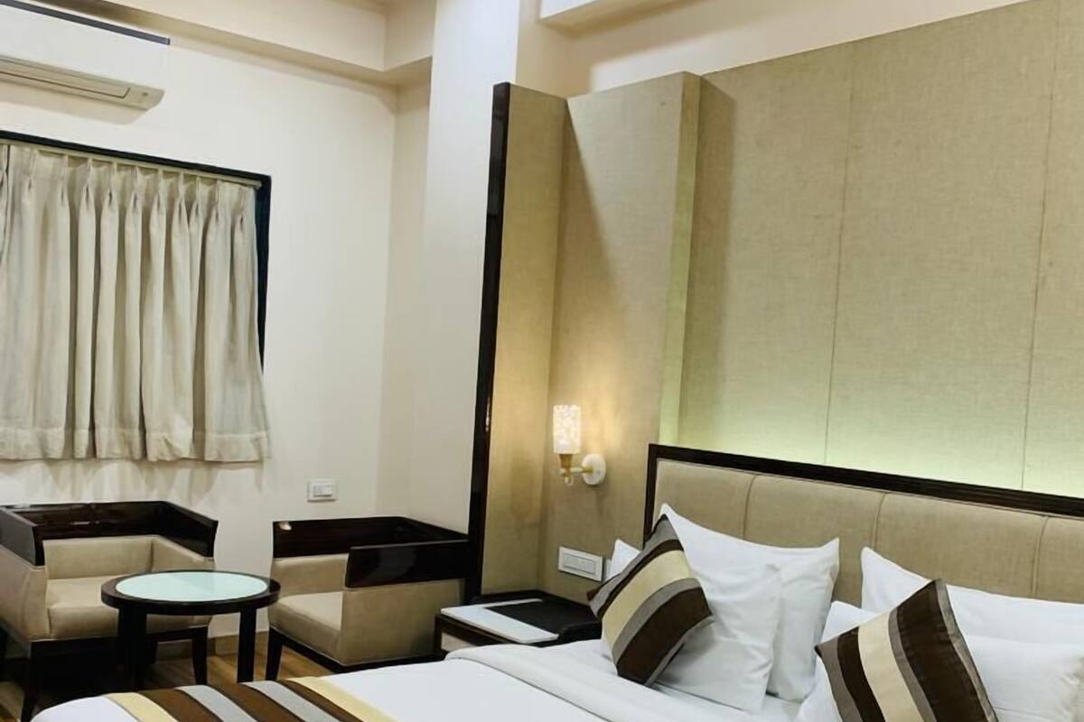 A hotel room with a large bed, two armchairs, a small table, a nightstand, and a mirror.