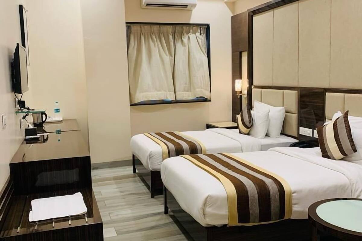 A hotel room with a large bed, a smaller bed, a desk, a mirror, an air conditioning unit, and a television.
