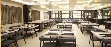 A spacious dining area with multiple tables and chairs, a modern ceiling design, and a logo in the upper right corner.