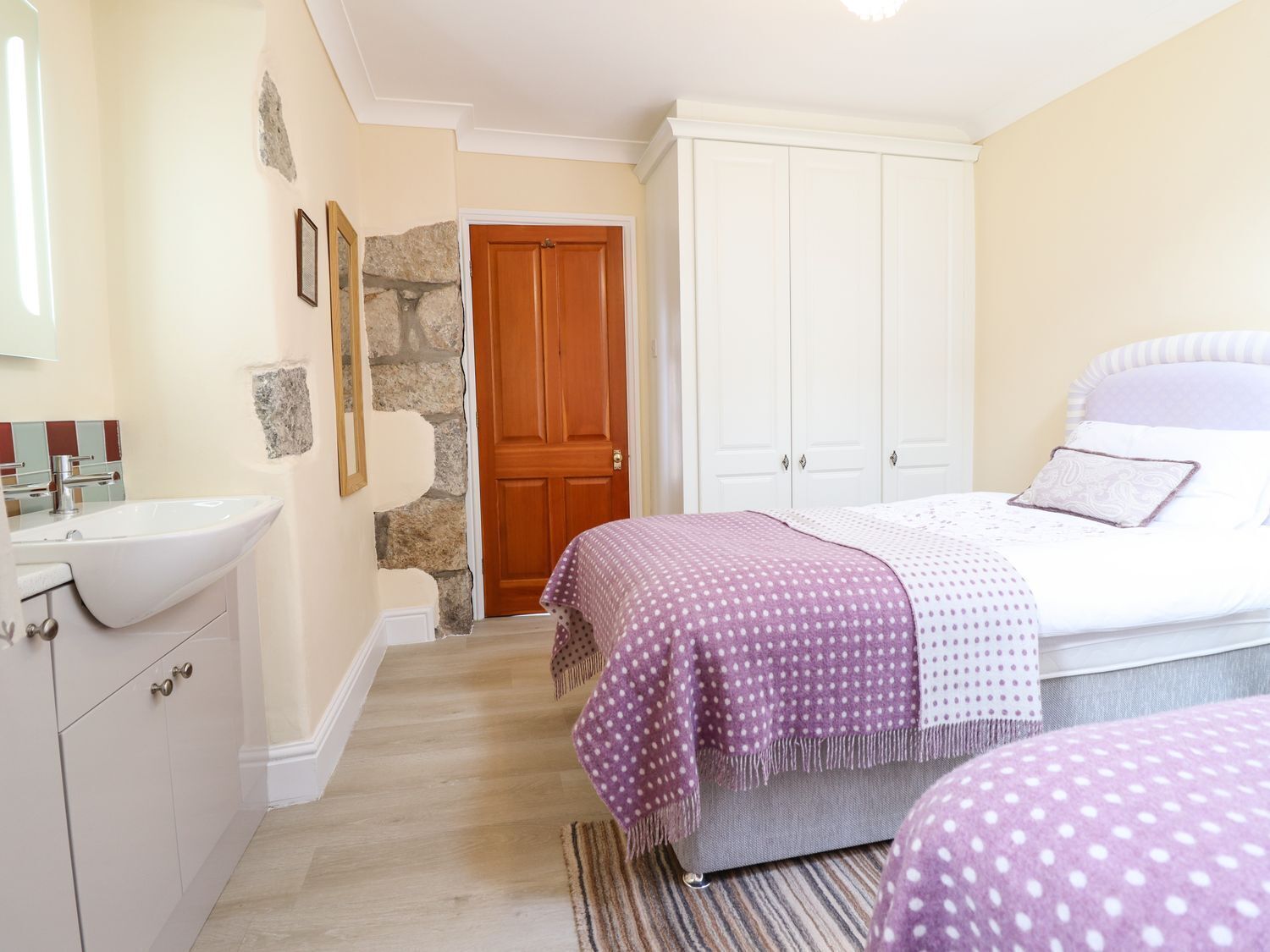 Une chambre à coucher comprenant un lit, une table de chevet, une commode et une salle de bain avec un lavabo et un miroir.