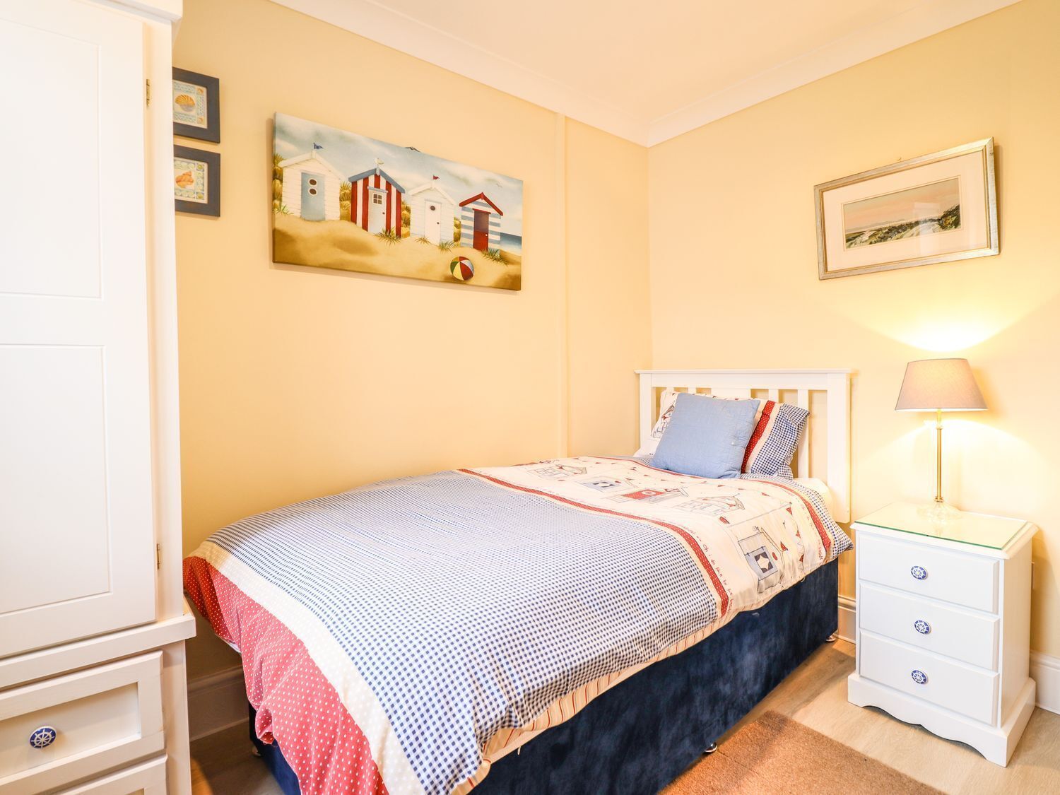 A bedroom with a bed, nightstand, dresser, and wall art.