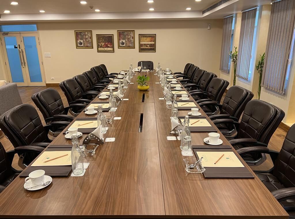 Un salón de conferencias con una larga mesa, sillas de cuero negro y suelo de madera.