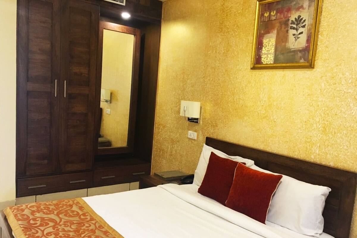 A hotel room with a bed, a wardrobe, a mirror, and a wall-mounted light fixture.