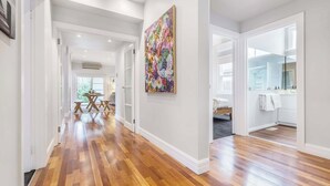 A spacious hallway with wooden flooring, a large colorful painting on the wall, and a view into a room with a bathtub and a mirror.