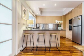 Uma cozinha moderna com armários de madeira, uma geladeira de aço inoxidável, um espaço com banquetas e uma janela com luminária.