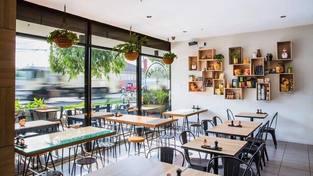 A modern restaurant with tables and chairs, hanging plants, and shelves with various items.