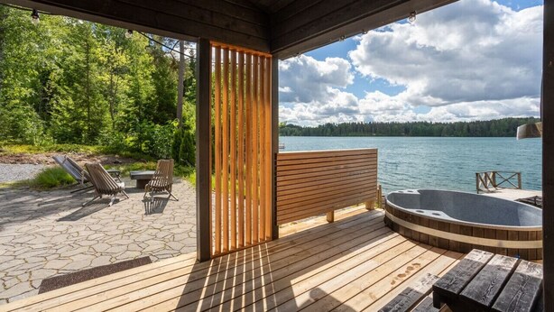 A wooden deck with a hot tub, lounge chairs, and a view of a lake.