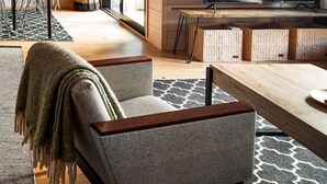 A modern living room with a wooden floor, a TV, a dining area with chairs and a table, and a large window.