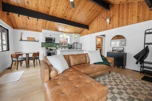 A spacious living area with a leather sofa, wooden ceiling, and a kitchen in the background.