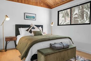 A bedroom with a bed, bedside lamps, a window with a snowy view, and a framed picture on the wall.