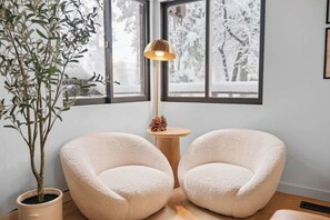 Ein gemütliches Zimmer mit zwei bequemen Sesseln, einem kleinen runden Tisch, einer Stehlampe und einem Topf mit Pflanze.