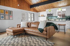 Ein modernes Wohnzimmer mit einem braunen Ledersofa, einem gemusterten Teppich und einer Holzbalkendecke.