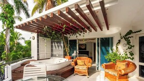 Een moderne buitenruimte met een jacuzzi, rieten meubilair en een pergola met hangplanten.