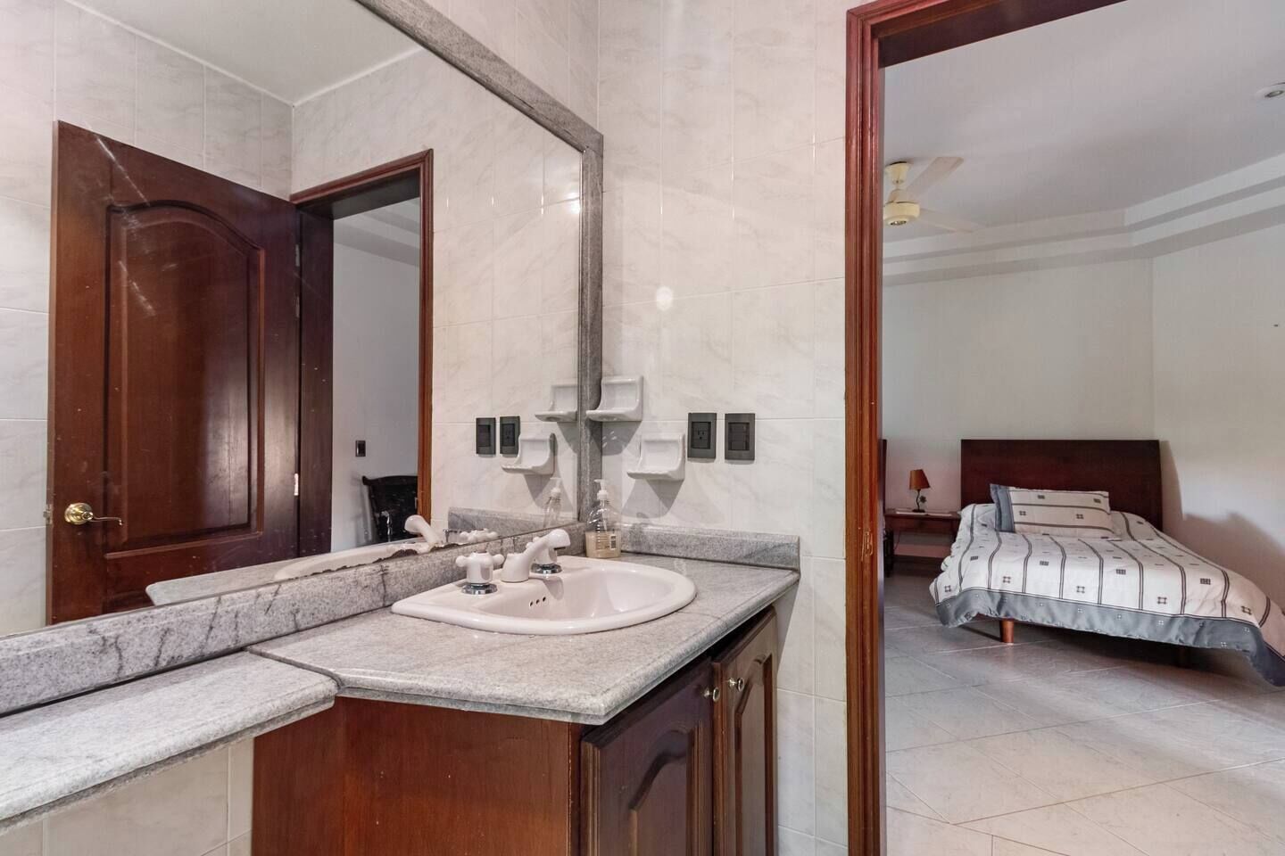 A bathroom with a marble sink, wooden cabinets, and a large mirror.