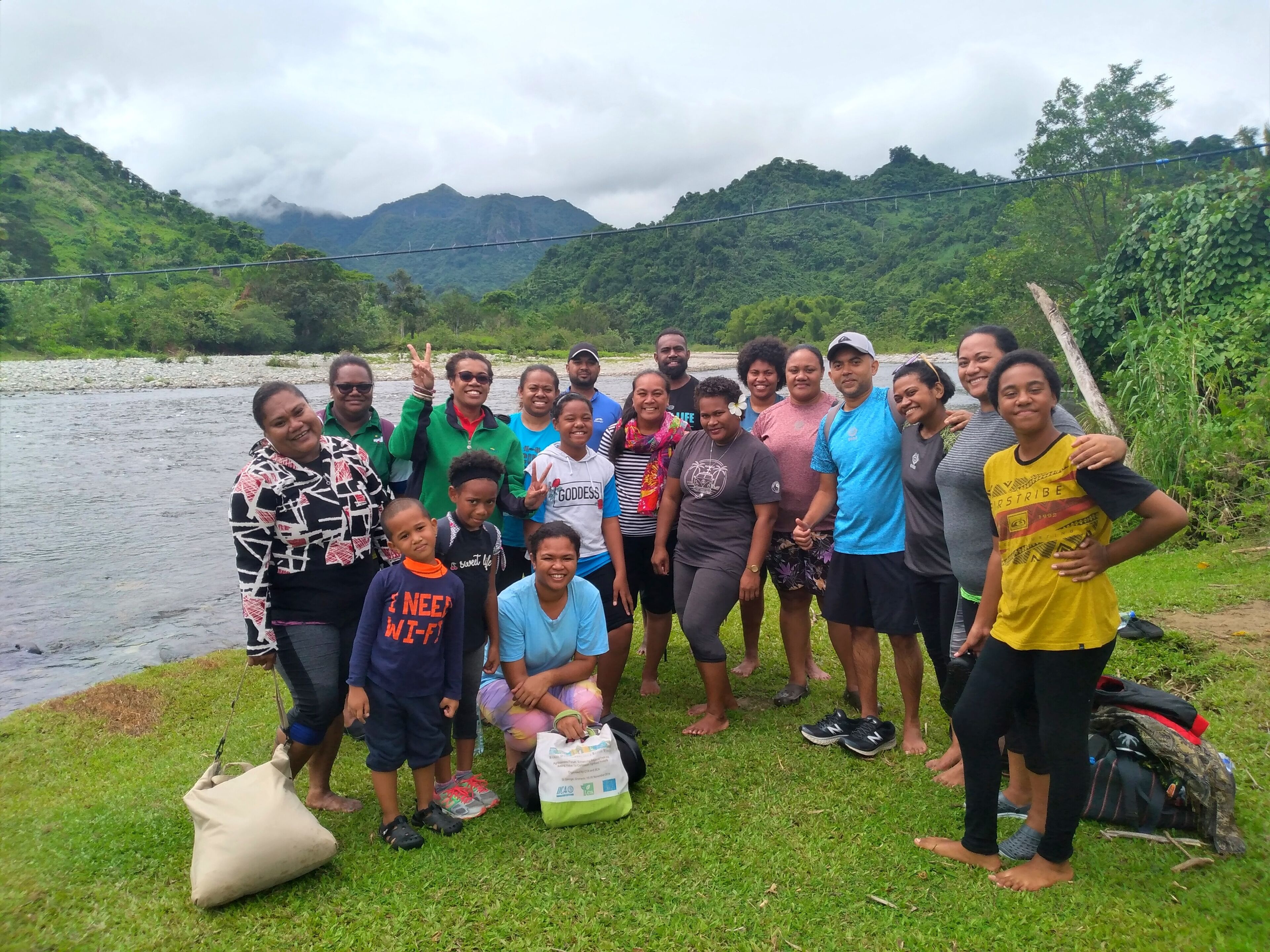 A group of people gathered by a river with mountains in the background.