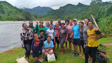 A group of people gathered by a river with mountains in the background.