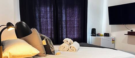 Habitación de hotel con cama, escritorio, lámpara, televisor y ventana con cortinas.