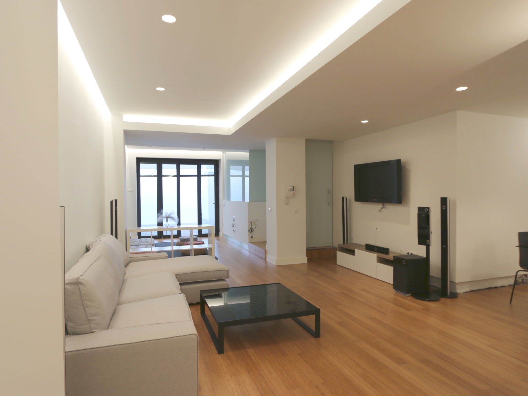 A modern living room with a sofa, a glass coffee table, and a TV mounted on the wall.