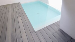 Un petit espace extérieur abritant une piscine, avec une terrasse en bois et un mur blanc.