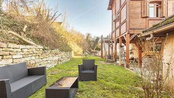 A courtyard with wicker furniture, a stone wall, and a wooden building with windows.