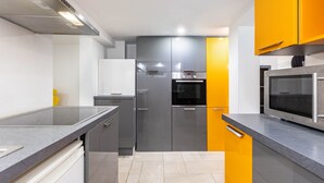Una cocina moderna con gabinetes grises y amarillos, electrodomésticos de acero inoxidable y encimera gris.
