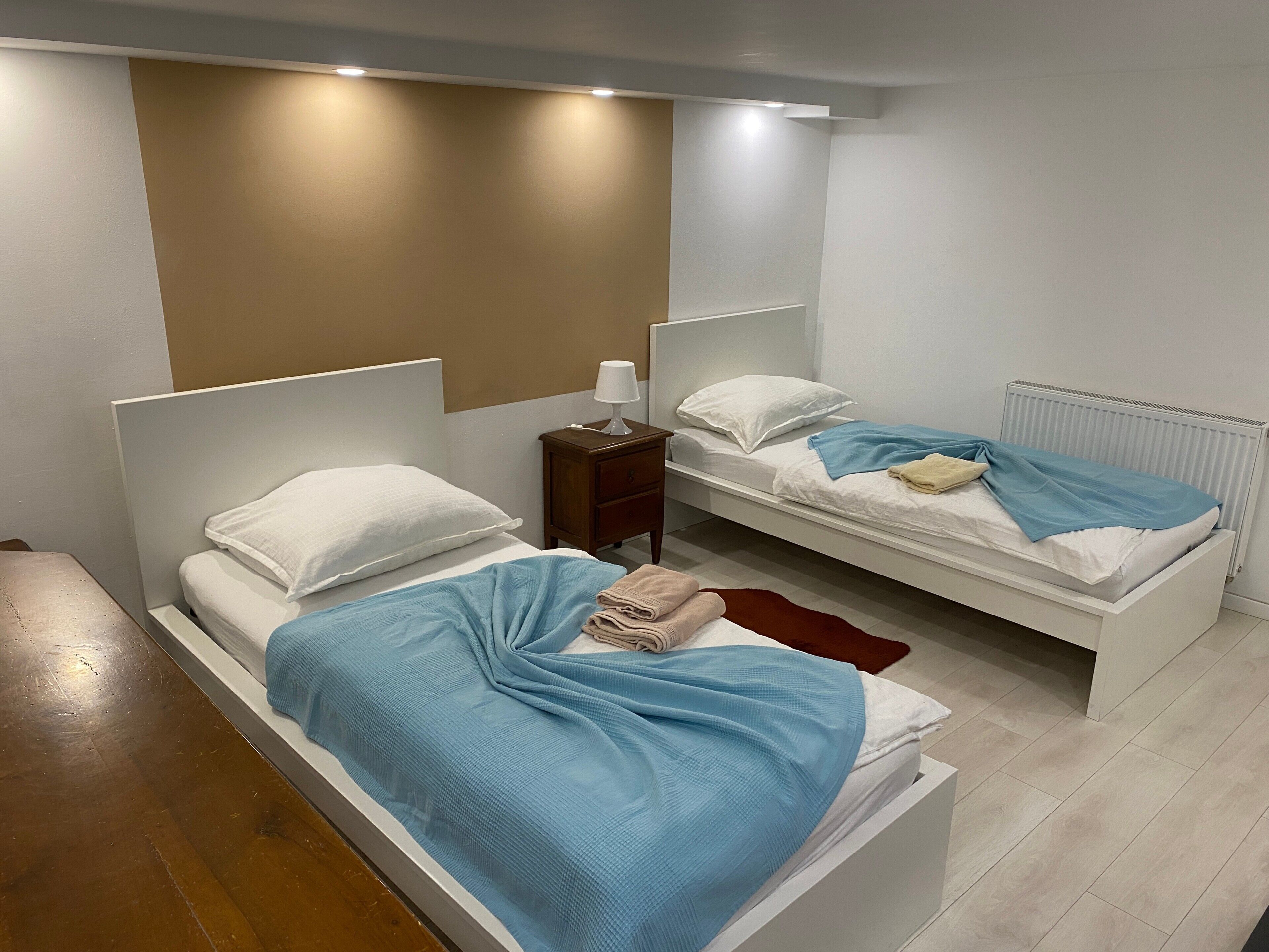 Quarto com duas camas, uma mesa de cabeceira, um abajur e um radiador.
