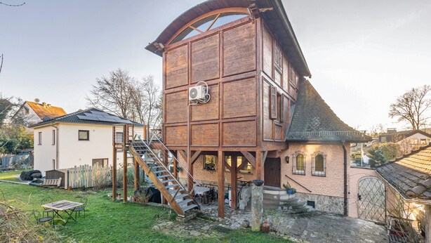 Una casa torre de madera con escalera, un camino de piedra y un pequeño jardín.