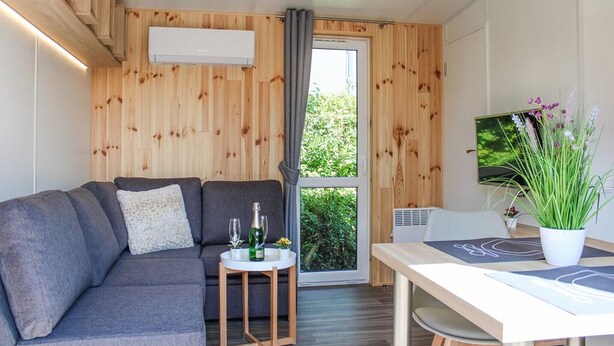 Une pièce moderne avec un canapé gris, une petite table sur laquelle se trouve un verre, et une plante en pot.