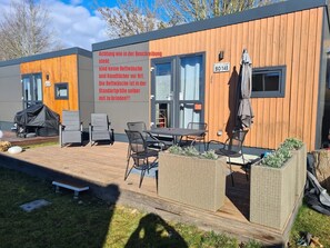 A modern building with a wooden exterior, a covered outdoor seating area with chairs and a table, and a sign indicating a standard-sized washing machine.