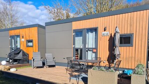 Un espace extérieur moderne aménagé avec une table et des chaises, un barbecue couvert et une terrasse en bois.