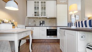 Una cocina compacta con armarios blancos, horno integrado, cafetera y una lámpara en la encimera.