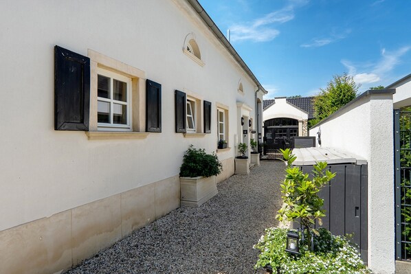 A narrow alleyway with a building featuring a series of windows with shutters, a gravel path, and potted plants. - Suite Maritim – Ground Floor Studio with Terrace by Offlumer See (Neuenkirchen)