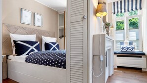 Un dormitorio con cama, mesita de noche, lámpara y ventana con contraventanas.