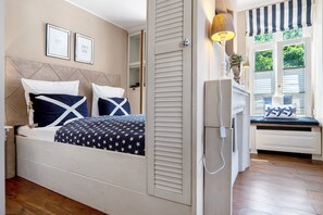 Un dormitorio con cama, mesita de noche, lámpara y ventana con contraventanas.