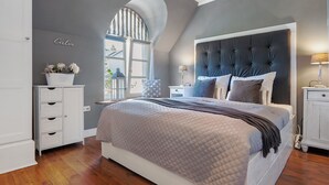Une chambre à coucher avec un grand lit, une commode, une table de chevet, une lampe et une fenêtre donnant sur un beau paysage.