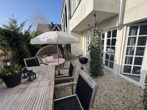 Eine Holzterrasse mit einem runden Tisch, Stühlen, einem Hängesessel und einem Sonnenschirm.