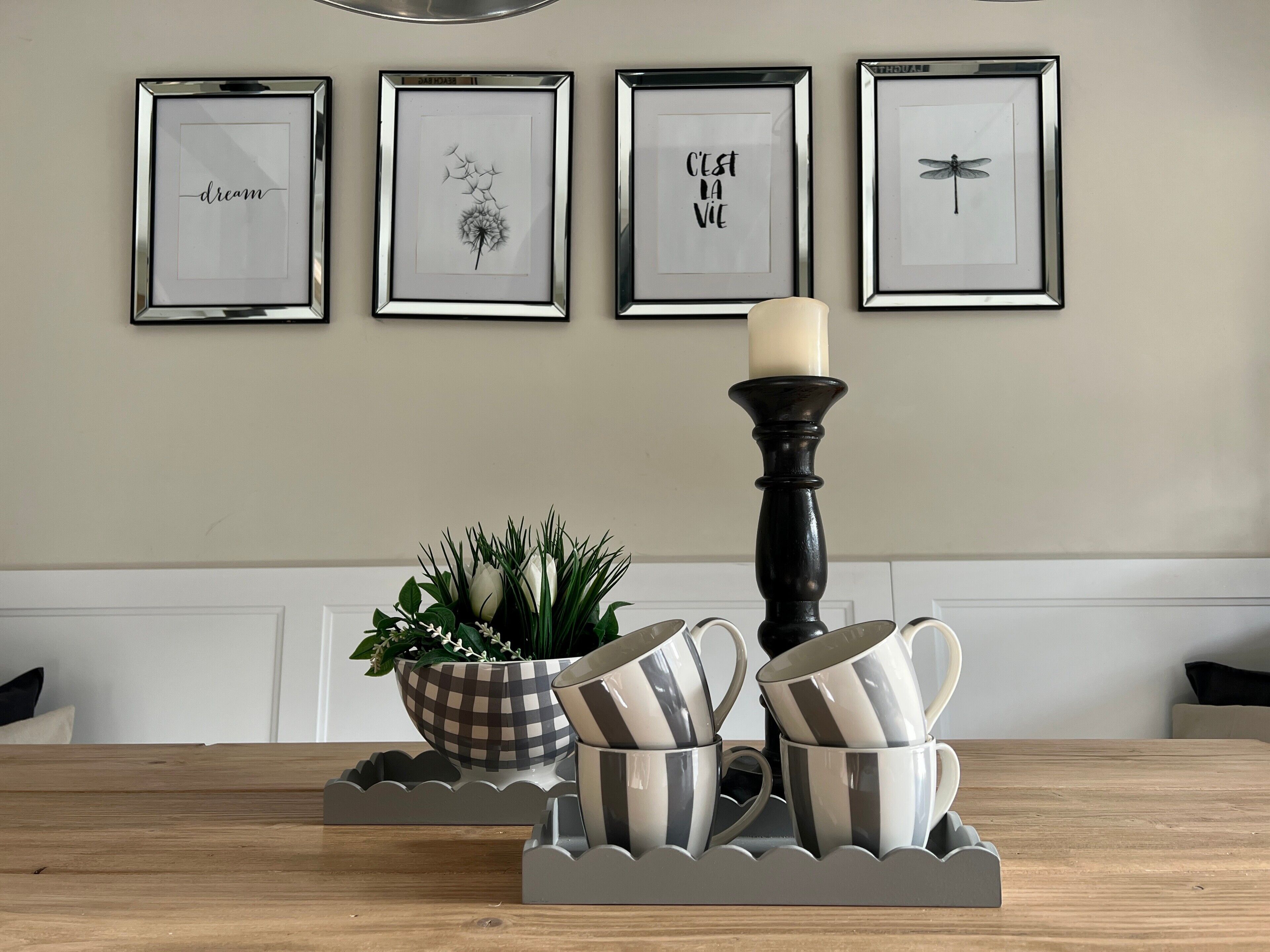 A dining table with a candle, a bowl of plants, and striped cups.