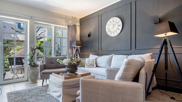 Un salon avec un canapé, un fauteuil, une table basse et une horloge au mur.