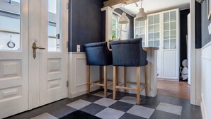 Une cuisine avec deux tabourets de bar, un sol à carreaux et une porte blanche.