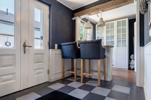 Een keuken met twee barstoelen, een geruit vloertje en een witte deur.