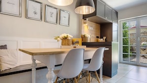 Une cuisine avec une table en bois, deux chaises, des œuvres d’art encadrées accrochées au mur et une vue à travers la porte vitrée.
