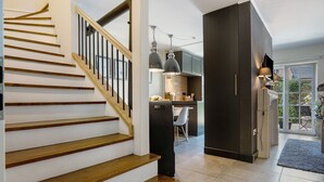 Un escalier avec des marches en bois et une rampe, menant à un espace cuisine équipé de placards et d’une table à manger.