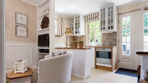Cocina compacta con armarios blancos, horno integrado y zona de comedor con una silla blanca.