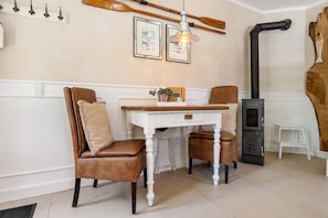 Quarto com uma mesa branca, duas cadeiras de couro marrom, um candeeiro pendente, um fogão preto e uma decoração de parede em madeira.