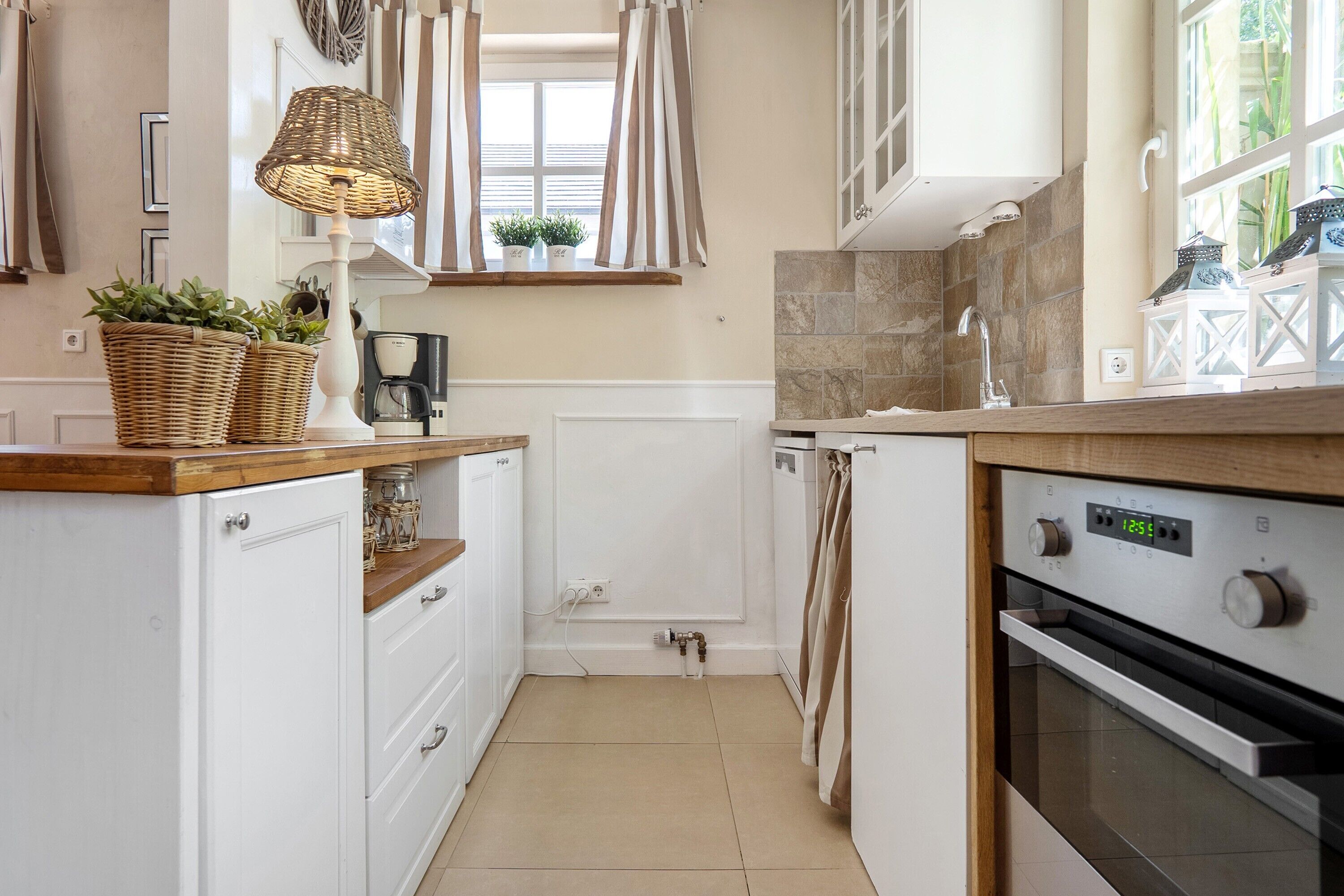 A kitchen with white cabinets, a wooden countertop, a built-in oven, and a window with curtains.