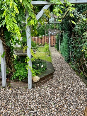 Un sentier de jardin agrémenté d’une pergola en bois, d’un chemin de gravier et d’une végétation luxuriante.