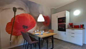 A dining area with a table set for two, a modern kitchen with appliances, and a large wall mural. - Holiday Apartment "Goldgrube - Ground Floor" with Private Terrace, Shared Garden and Wi-Fi (Koblenz)