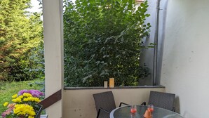 A patio with a round table and chairs, a potted plant with yellow flowers, and a large leafy plant in the background. - Holiday Apartment "Goldgrube - Ground Floor" with Private Terrace, Shared Garden and Wi-Fi (Koblenz)