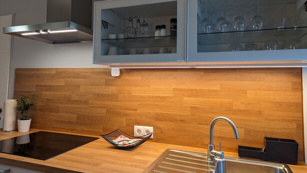 A modern kitchen with a wooden backsplash, a built-in oven, a sink with a faucet, and a glass-fronted cabinet above the countertop. - Holiday Apartment "Goldgrube - Ground Floor" with Private Terrace, Shared Garden and Wi-Fi (Koblenz)