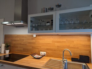 Uma cozinha moderna com painel de madeira, forno embutido, pia com torneira e armário com porta de vidro sobre a bancada.